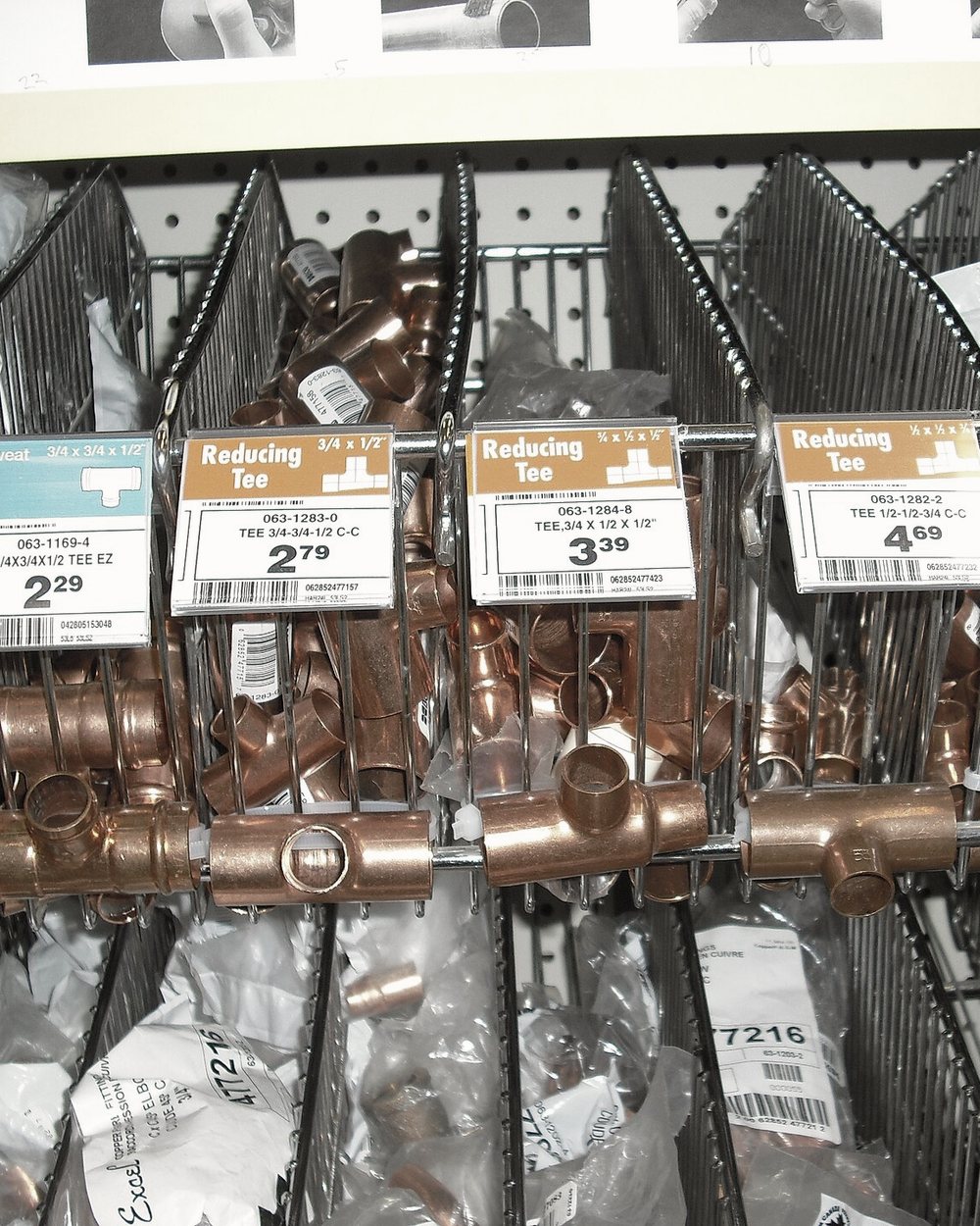 Bins of copper tees and reducing fittings with shelf price labels.