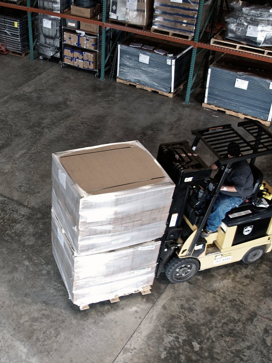 A forklift moving a wrapped pallet past stocked racking.